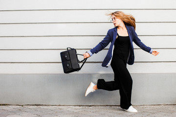 Business woman running in a suit with a briefcase along the wall.