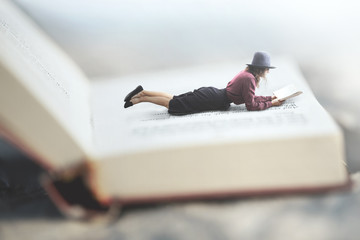 surreal situation of a woman reading her book lying on a giant book