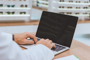 partial view of optician using laptop with blank screen in optica