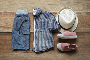 Fashionable concept, children’s clothes with sneaker, shirt, pants, eyeglasses and hat on wooden background. pack shots, top view