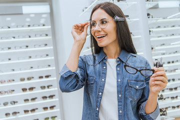 smiling attractive woman choosing eyeglasses in optics