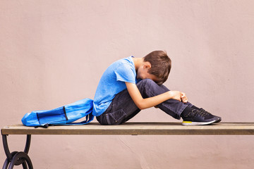 Sad, tired child sitting alone on the bench outdoors.