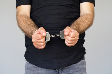Close-up. Arrested man handcuffed hands isolated on gray background. Prisoner or arrested...