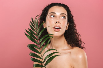Naklejka premium Beautiful young woman posing isolated over pink take care of her skin holding leaf.