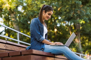 Amazing young beautiful woman sitting outdoors using laptop computer.