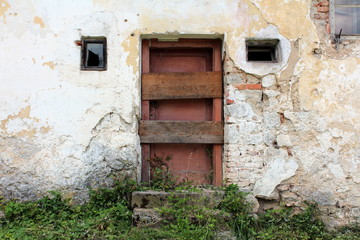 Dark red wooden doors with boards nailed across on abandoned dilapidated brick house with two small...
