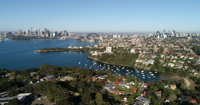 Small secluded bay on Sydney harbour at Lower North Shore with floating yachts seen from above in view of distant city CBD landmarks and North Sydney.

