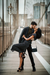 Love story in New York. Man and exotic woman dance with passion on the street with Brooklyn bridge behind them