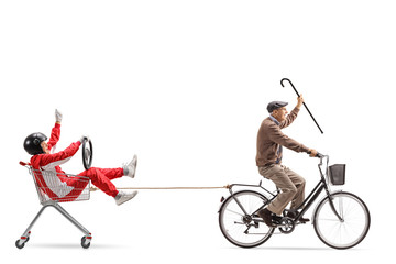 Elderly man with cane riding a bicycle and pulling a shopping cart with a man in a racing suit