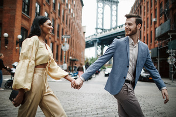 Love story in New York. Indian woman in bright yellow clothes and handsome American man hold each other hands walking around the New York