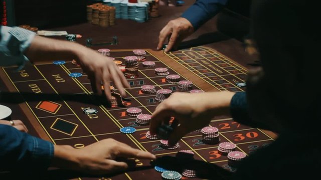Players hands betting on roulette table. Casino gambling table brown surface with classic betting grid. Close up human hand puts down casino chips on sectors with numbers. Gambling game in casino