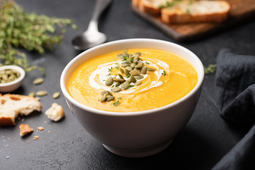 Pumpkin cream soup in bowl on black concrete background. Closeup view, selective focus. Autumn comfort food concept