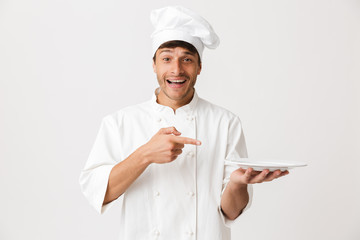 Handsome young chef isolated over white background holding plate.