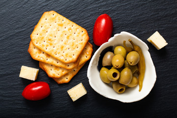 Food Appetizer Olives cheese, tomatoes and cracker on black slate board with copy space