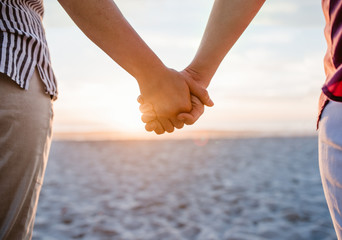 Loving lesbian couple holding hands on a beach at sunset