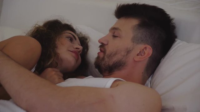a pair of lovers lying in bed, kissing and talking. The funny girl hugs her beloved and laughs . a strong man takes a woman. earlier morning in hotel room 4K