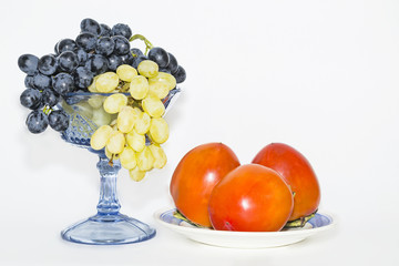 persimmon on a plate and grapes in a vase