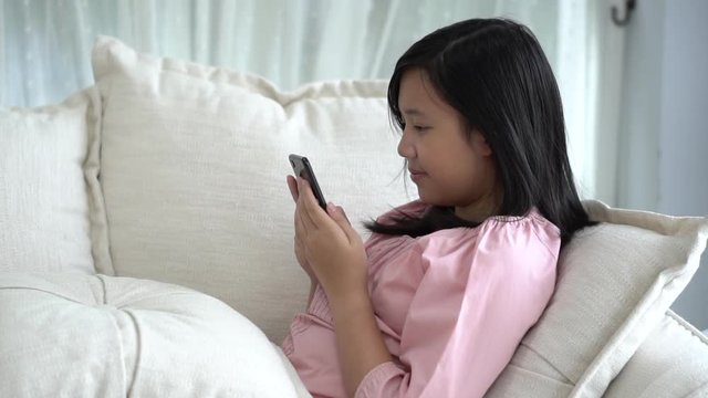 Beautiful Asian girl playing smartphone  sitting on a sofa in the living room at home slow motion 