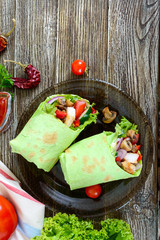 Burrito with chicken, vegetables, mushrooms in pita bread with spinach on a wooden table. Mexican food.