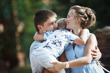 Young happy family: father, mother and blond boy walking in the park.