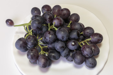 Branch of a red grape on the white plate. Vegan food.