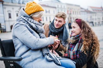 Two teenagers giving a present to a grandmother in wheelchair outdoors in winter.