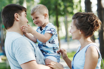 Fototapeta premium Young happy family: father, mother and blond boy walking in the park.