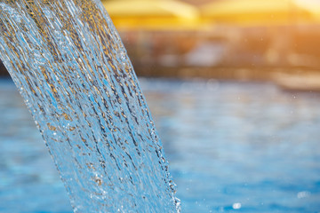 Stream of water in the pool. Blue surface, spray, close-up. Selected focus.