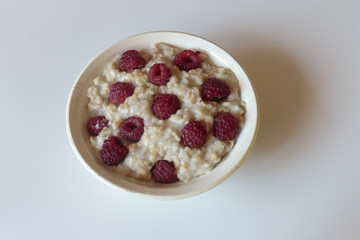 Hot oatmeal porridge with cream and fresh raspberries. Healthy breakfast concepts.