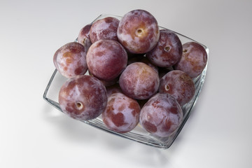 Ripe fresh plums in a glass dish over the white background. Vegan food.