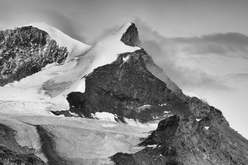 B&W close-up of Adlerhorn with glacier Adlergletscher after light snowfall with forming clouds
