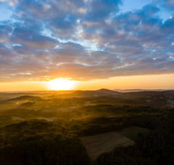 Aerial view of sunrise in foggy morning, forest and field in the foreground, view from air