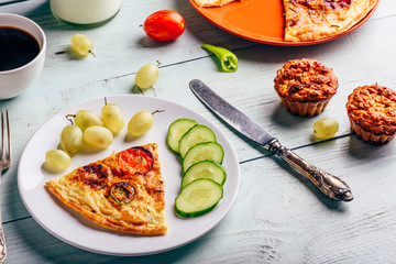 Slice of frittata with cup of coffee, grapes and muffins.