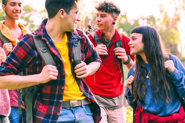 Happy young friends hiking with positive attitude - Cheerful group of teenagers smiling looking at each other holding trek backpack - Concept of friendship, travel and outdoor activity - Focus on girl