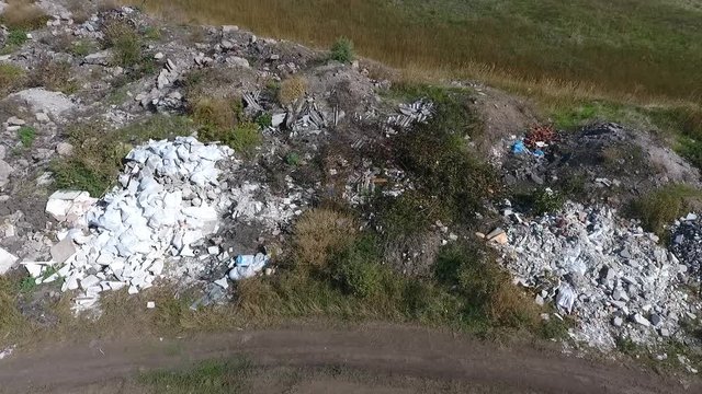 The drone flies sideways at low altitude. Heaps of construction and household garbage left by people are clearly visible. We see pieces of plasterboard, slate, bricks, bags, old tires..