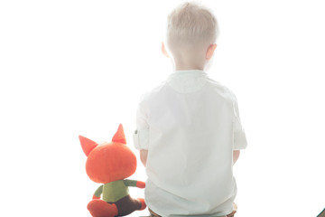 a little boy is sitting with his back to us plays with a toy Fox