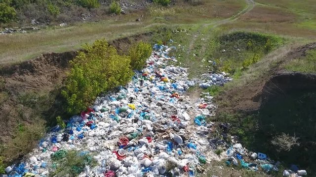 A big pile of garbage in the pit. Environmental pollution. Sunny day. Everywhere garbage and waste. People throw garbage on the ground.  Many colored bags, plastic, bottles and other waste..