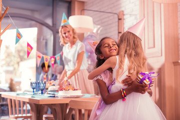 Cute little girls. Cheerful kind girl hugging her best friend while greeting her at the birthday party