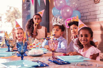 Five children. Positive relaxed pretty kids sitting together at the birthday party and blowing...