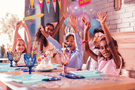 Excited Friends. Cheerful Excited Kids Visiting Great Birthday Party And Smiling While Putting Their Hands Up