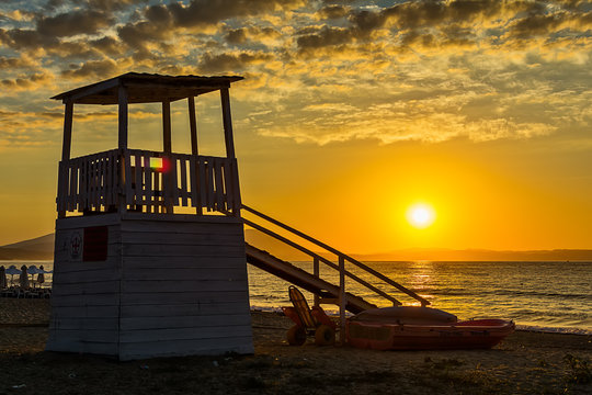 Early morning, dramatic sunrise over sea and house for rescuers on the beach.