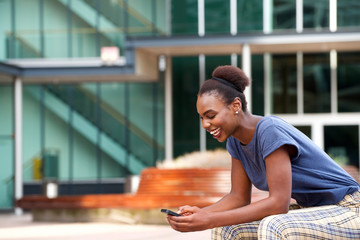 Side portrait of young african american woman looking at mobile phone outdoors