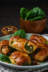 Spinach croissants with raisins, pinions and goat cheese and with a bowl of spinach on the plate with dark background. Space for text, vertical. Healthy concept.