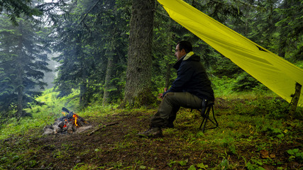 Camper man sitting in front of a campfire in the rain