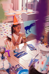 Theme party. Thoughtful long haired girl wearing party hat and calmly drinking juice
