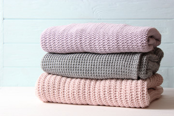 A pile of warm sweaters on a wooden table on a light background. Autumn and winter clothes.