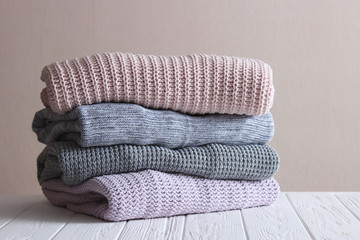 A pile of warm sweaters on a wooden table on a light background. Autumn and winter clothes.