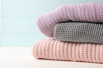 A pile of warm sweaters on a wooden table on a light background. Autumn and winter clothes.