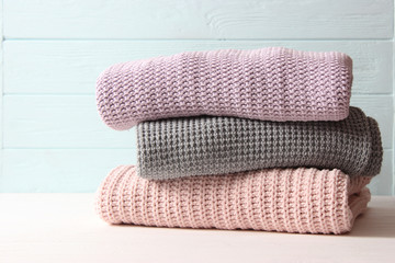 A pile of warm sweaters on a wooden table on a light background. Autumn and winter clothes.