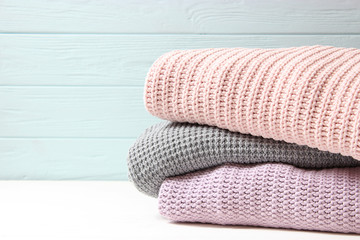 A pile of warm sweaters on a wooden table on a light background. Autumn and winter clothes.